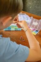 Focused on his project, a boy strings together colorful beads to create a bracelet, using materials spread out before him. photo