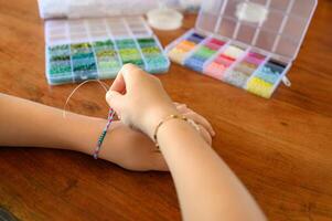hands crafting a beaded bracelet at home, with vibrant beads laid out neatly in small containers on the table. photo