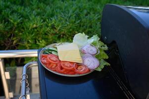 Plates filled with fresh vegetables and cheese are resting on the grill, ready to be used for assembling burgers photo