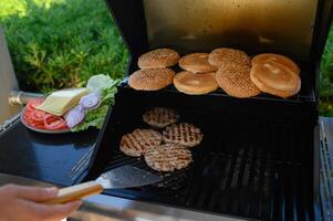 Perfect summer barbecue moment grilling burgers, assembling them with crisp toppings, securing with sticks, and ketchup set nearby for serving. photo