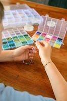 Little hands working patiently on a handmade bracelet, with a table full of colorful beads and crafting supplies. photo