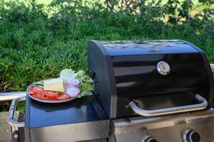 A backyard grill loaded with burger patties and buns, next to a plate full of colorful fresh ingredients for assembling classic burgers. photo