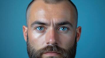 Man with striking blue eyes and beard against a solid blue background, capturing a moment of intense expression and focus photo