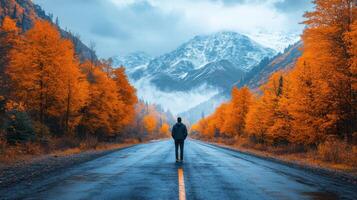 Person walking on a wet road through colorful autumn trees with mountains in the background photo