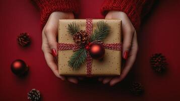 Christmas gift wrapped in festive paper held by hands on a red background surrounded by decorations photo