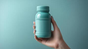 Hand holding a teal bottle against a soft blue background during daylight photo