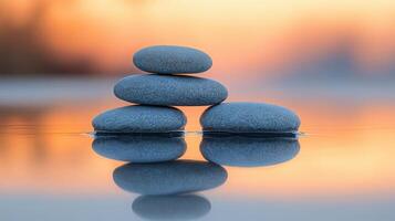 Stacked smooth stones reflecting on still water during sunset with warm orange and yellow hues in the background photo