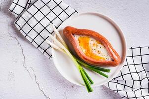 Close up of fried egg in a sausage in the form of khachapuri on a plate on the table top view photo