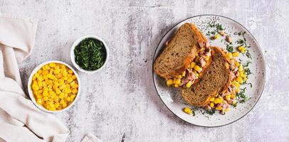 Tuna and corn salad on grain bread on a plate on a table top view web banner photo