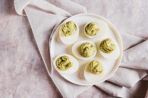 Close up of eggs stuffed with avocado and yolk mixture on a plate on a table top view photo