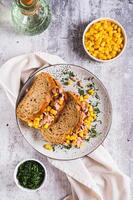 Tuna and corn salad on grain bread on a plate on a table top and vertical view photo