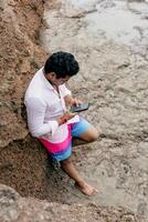 Photo from above of a stylish man at the beach using his smartphone, vertical shot with copy space