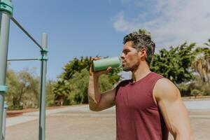 A man is drinking from a bottle during a break while he is working out, hydration in sport in sport photo