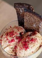 Scoops of artisanal ice cream sprinkled with freeze dried raspberry crumbles and topped with crispy rye bread in a glass bowl, offering a unique and contrasting flavor combination photo