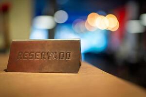 Metal reservado sign sitting on wooden restaurant table, marking reserved seating with soft background blur creating delicate bokeh lighting effect photo