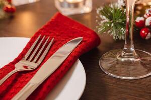 Christmas table setting. Plate and cutlery on napkin. Preparing for festive dinner. Candles burning on table on Christmas Eve photo
