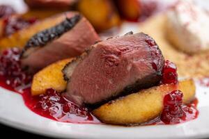 Close up of juicy, seared duck breast, served with roasted peach slices, tart cranberry sauce, and creamy polenta, offering a delightful combination of flavors and textures photo