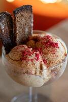 Delicious rye bread ice cream decorated with freeze dried raspberries served in an elegant glass bowl, placed on a wooden table in front of a warm blurred background with orange bokeh.. photo