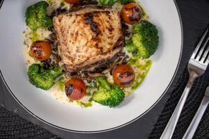 Grilled fish fillet resting on a white plate, accompanied by wild rice, tender broccoli, and roasted cherry tomatoes, creates a visually appealing and nutritious meal, perfect for fine dining photo