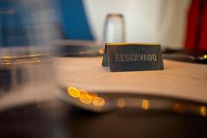 Metal reserved sign standing on an elegant restaurant table, creating an inviting atmosphere with soft, warm lighting and blurred tableware in the foreground and background photo