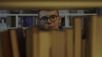 A thoughtful reader sits in a library, surrounded by books and shelves, engaging in reflection. Media photo