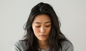 Young woman with long dark hair looking down, expressing deep thoughts and emotions, captured in a minimalist setting, introspective mood, mental health concept photo
