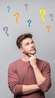 Young man pondering questions with colorful symbols above his head, deep in thought about life choices and decisions, curiosity and contemplation concept photo