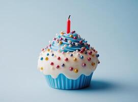 Blue-frosted cupcake sporting colorful sprinkles and single glowing candle resting on vivid blue surface, marking birthday festivity photo
