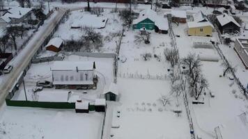 Aerial view of a serene snowy village with quaint houses, snow-laden rooftops, and a winding dirt road, capturing winter solitude amidst a fresh white blanket and bare trees dusted with snow video