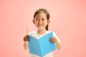 Joyful First Grader Girl Reader with Exercise Book Against Pink Isolated photo