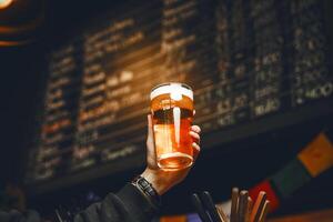 Hand Holding Beer Glass in Lively Bar With Menu Stand in Background photo