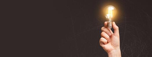 A hand holding a light bulb over a dark background photo