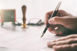 Man signing a contract with pen and paper on desk photo
