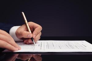 A man in a suit is signing a document with a pen photo