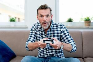 A man is sitting on a couch holding a game controller photo