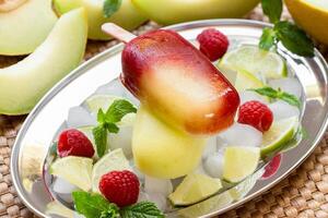 Delicious melon raspberry ice cream is displayed on a silver tray, surrounded by ice, fresh raspberries, lime slices, and mint leaves, perfect for a hot summer day. photo
