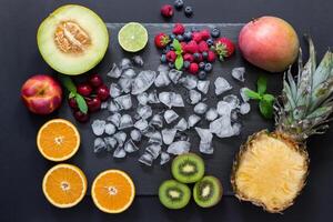 Rectangle of pineapple, mango, kiwi, oranges lime, melon, nectarine and cherries strawberries, blueberries, raspberries in center ice cubes on black background. Fruits berries rectangle. Horizontal. photo