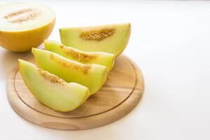 Fresh cantaloupe slices arranged neatly on a wooden cutting board, with the whole fruit beside them. The yellow rind contrasts with the juicy green flesh, making it an appealing summer treat. photo