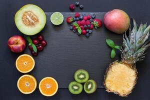 Rectangle of pineapple, mango, kiwi, oranges lime, melon, nectarine and cherries strawberries, blueberries, raspberries in center empty space on black background. Fruits berries rectangle. Horizontal. photo