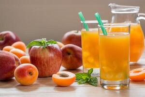 Apricot peach apple juice in glasses with ice near jar of juice and scattered apricots, peaches, apple, mint on a light wooden background. Apricot peach apple juice with ice. Horizontal. Daylight. photo