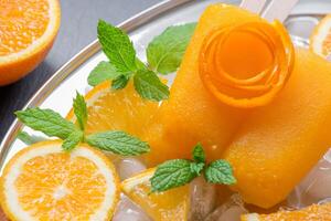 Bright orange ice cream is beautifully presented on a plate with refreshing orange slices and mint leaves, creating a perfect summer treat. Enjoying this dessert brings joy and freshness. photo