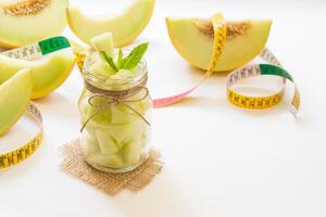 Left a jar with melon pieces on burlap napkin near cut slices of melon and centimeter right empty place for text on a white background. Pieces of melon in a jar. Horizontal. Daylight. photo