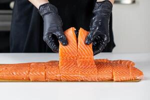 fresh salmon fillet slices being prepared by a chef in black gloves on a white surface photo