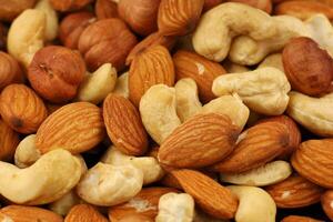 Nuts of various types including almonds, cashews, hazelnuts, and peanuts arranged closely together on a wooden surface photo