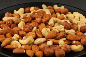 Mixed nuts assortment on a black plate with almonds, cashews, and hazelnuts arranged for snacking options photo