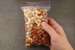 Mix of assorted nuts in a clear bag held by a hand against a neutral background in a kitchen setting photo