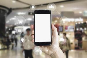 Hand holding smart phone device with isolated on white blank screen mobile phone with blur background image of shopping mall or department store with bokeh photo