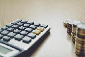 Money coins stack, calculator and some stationery on wood table, top view with copy space. Accounting and financial economic Math calculation concepts photo