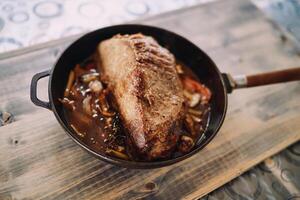 Frying pan with roast beef with vegetables stands on a wooden table photo