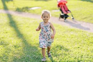 Little girl walks smiling along the green lawn from the stroller on the path photo